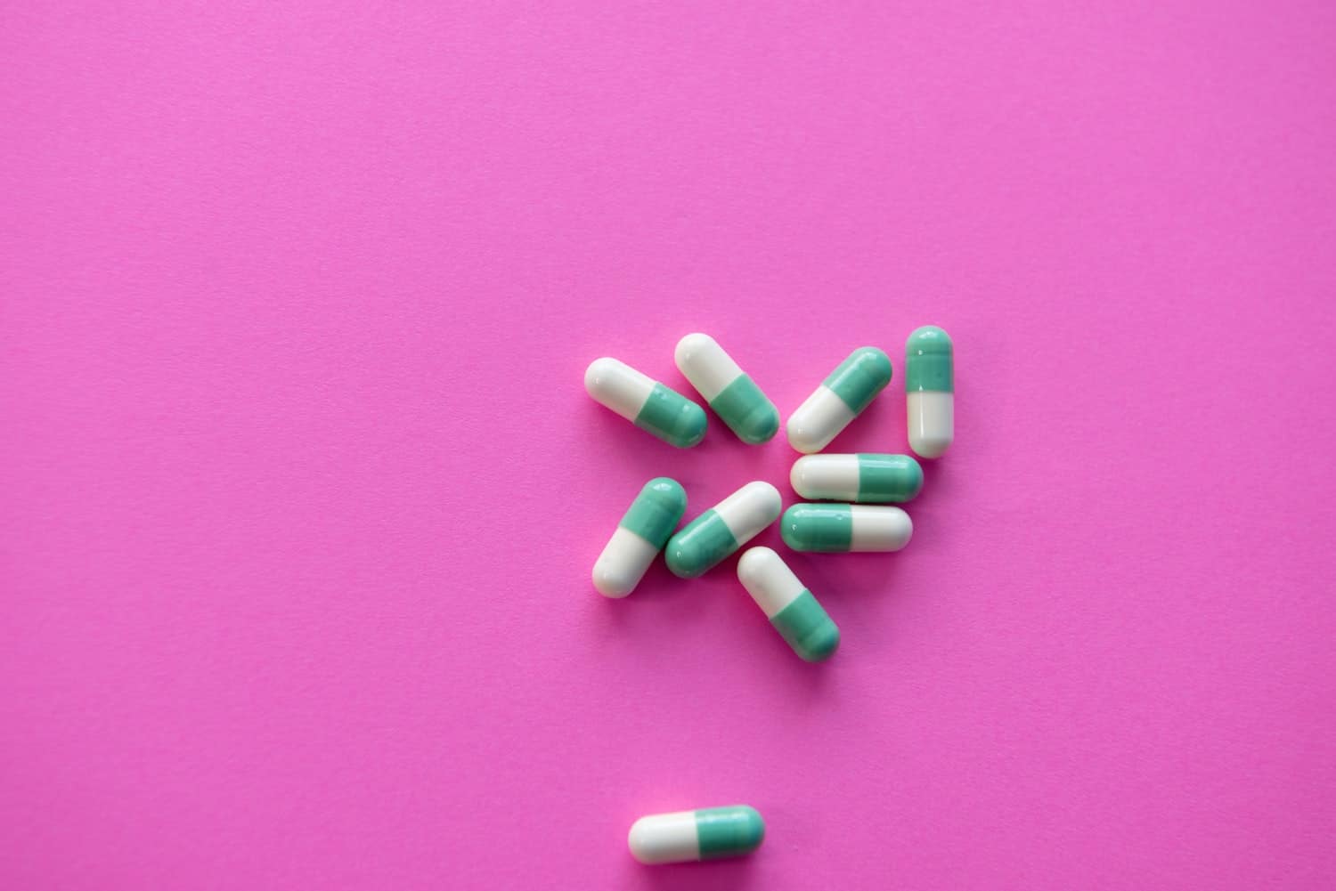 A small pile of over-the-counter pain relievers on a pink background.