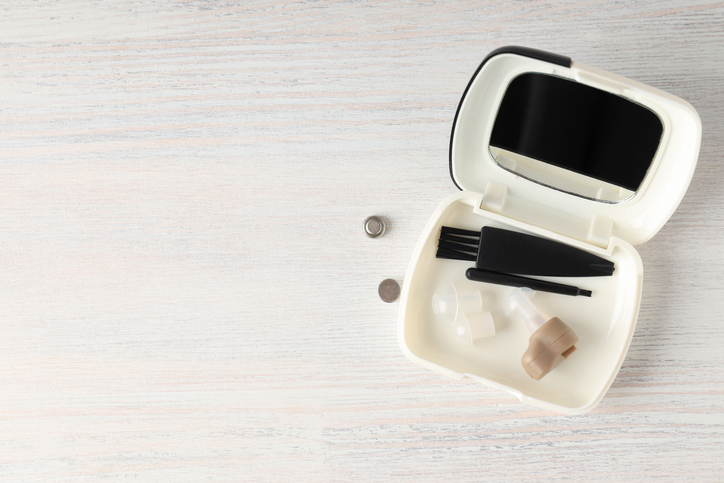 hearing aid cleaning tools next to hearing aid on wooden surface.